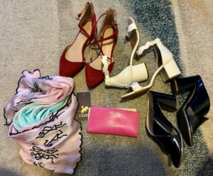 A picture of three heel one red, one white and one black and a colored scarf and a pink wallet. 