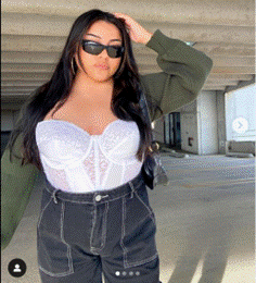 Women with a long hair wearing sunglasses. a white top, a green cardigan and black pants.