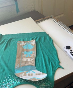 A picture of a teal sweater and a stocking shape stencil on top of it.