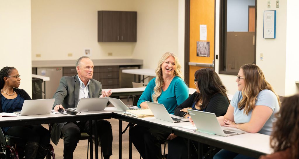 Group of professionals seated around a conference table with laptops, engaged in a lively meeting.