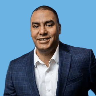 Smiling man wearing a navy checkered blazer and white shirt against a blue studio background.