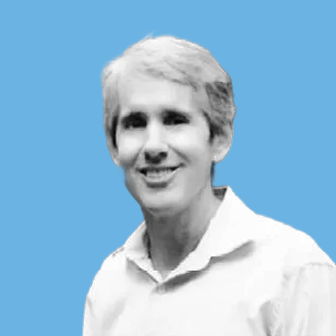 Person with short light hair wearing a white collared shirt against a solid blue background.