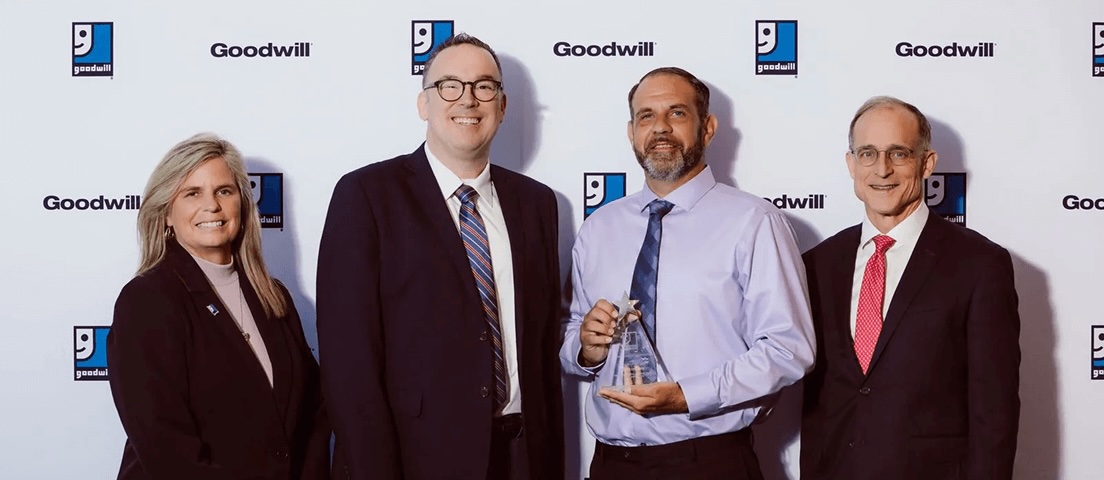 Four professionals posing with an award at a Goodwill event, backdrop featuring Goodwill logos.