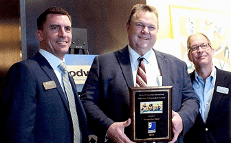 Three men in business suits at an awards ceremony; one holds a framed plaque.