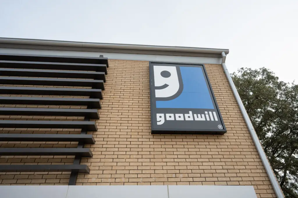 Goodwill storefront sign mounted on a beige brick wall with a blue square logo.