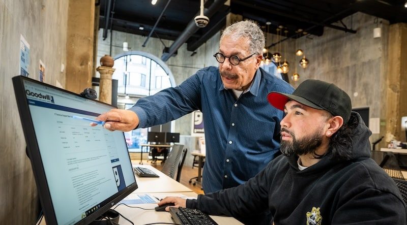Mentor points to a large computer screen while a student watches in a modern office.