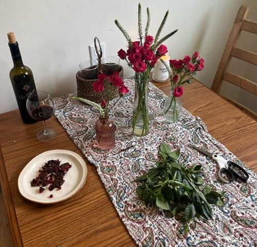 Picture of a wood table with a runner, flower vases with red flowers and a plate.