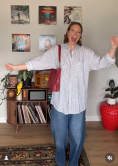 A picture of a women cheering wearing jeans pants a blue stripped blouse holding a red purse