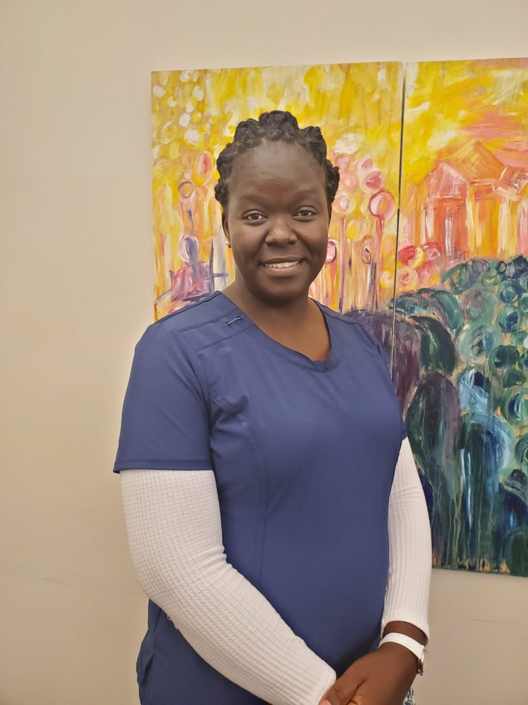 African American nurse in blue scrubs standing in front of a colorful abstract painting.