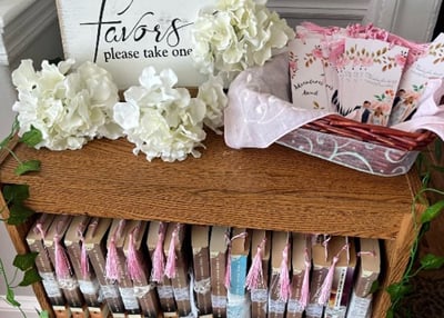 Pastel party favors displayed on a wooden crate with white hydrangeas and a 'favors please take one' sign.