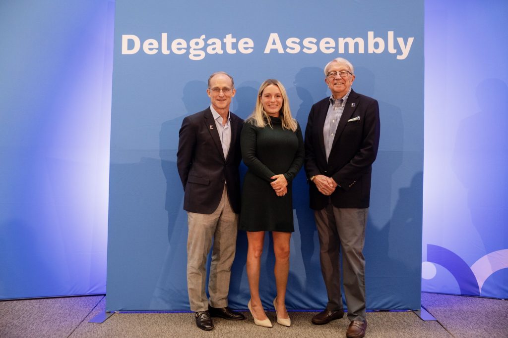Three people pose in front of a blue Delegate Assembly backdrop.
