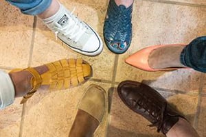 A circle of diverse footwear arranged on a tiled floor.