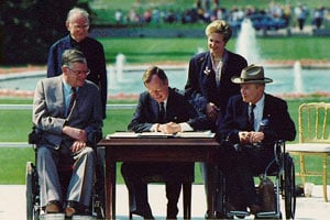 President George H. Bush signs the ADA in 1990, witnessed by Rev. Harold Wilke, Evan Kemp, Justin Dart and Sandy Parrino. President George H. Bush signs the ADA in 1990, witnessed by Rev. Harold Wilke, Evan Kemp, Justin Dart and Sandy Parrino.