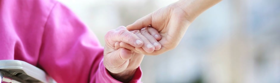 Close-up of two hands clasped together, one younger hand holding an elderly person's hand.
