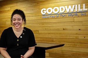 Smiling woman seated in front of a light wood panel wall with the Goodwill logo visible.