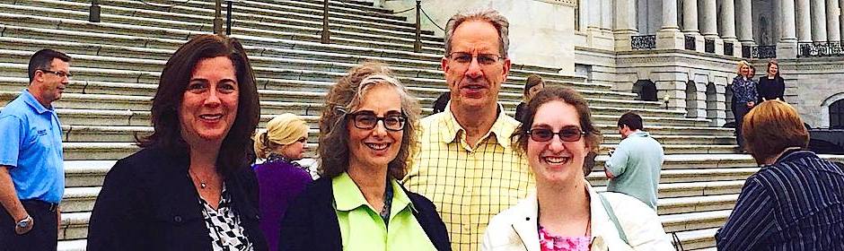 Four adults posing on wide stone steps in front of a grand neoclassical building, smiling at the camera.
