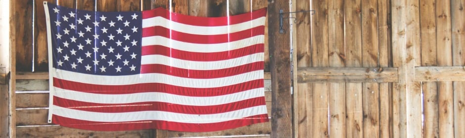 United States flag hanging on a weathered wooden barn wall.
