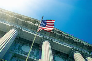 American flag waving in front of a neoclassical government building with tall stone columns.