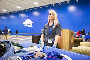 Volunteer with lanyard standing by piles of donated clothes in a bright donation center.