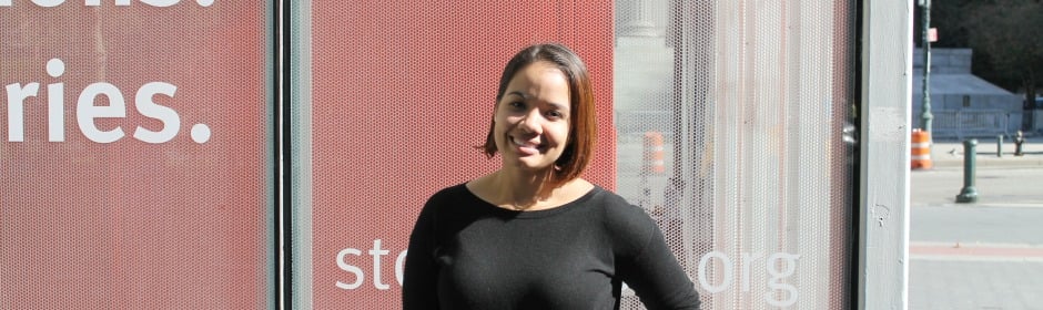 Smiling woman in a black top stands in front of a red panel with white text.