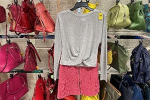 Boutique display featuring a grey sweater and pink skirt on a hanger, surrounded by colorful handbags.