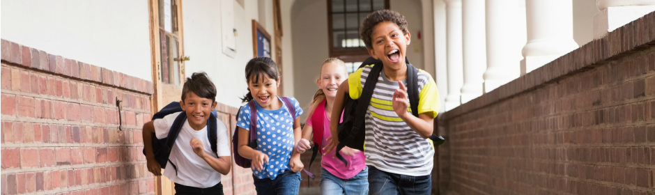 Diverse group of children running toward the camera in a school hallway with backpacks.