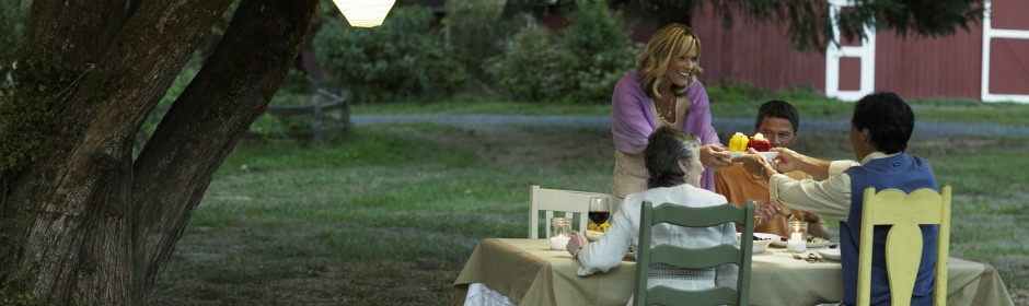 A group of friends dining outdoors under a large tree at dusk, sharing a toast.