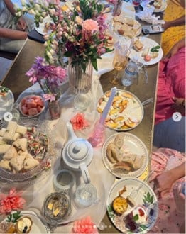 Brunch table with a floral centerpiece, pastries, fruit bowls, teapots, and colorful drinks.