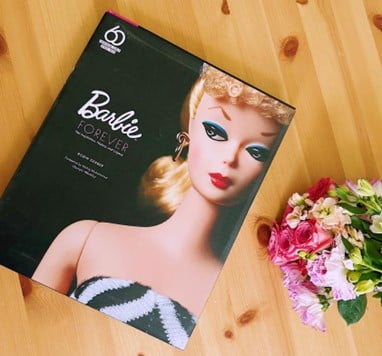 Barbie Forever box featuring a glamorous blonde doll with teal eyeshadow on a wooden floor beside a bouquet.