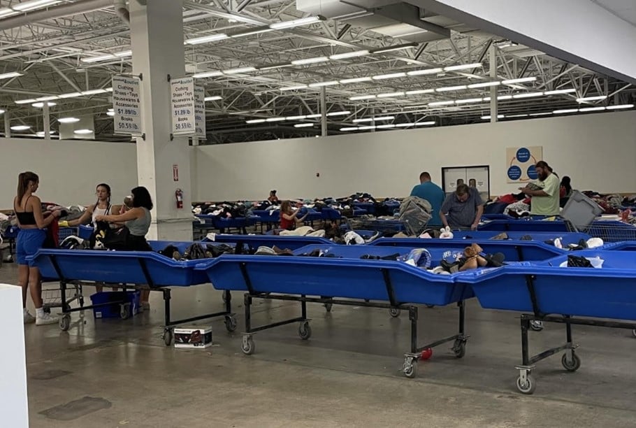 Volunteers sort donated clothing in a large warehouse with blue rolling bins.