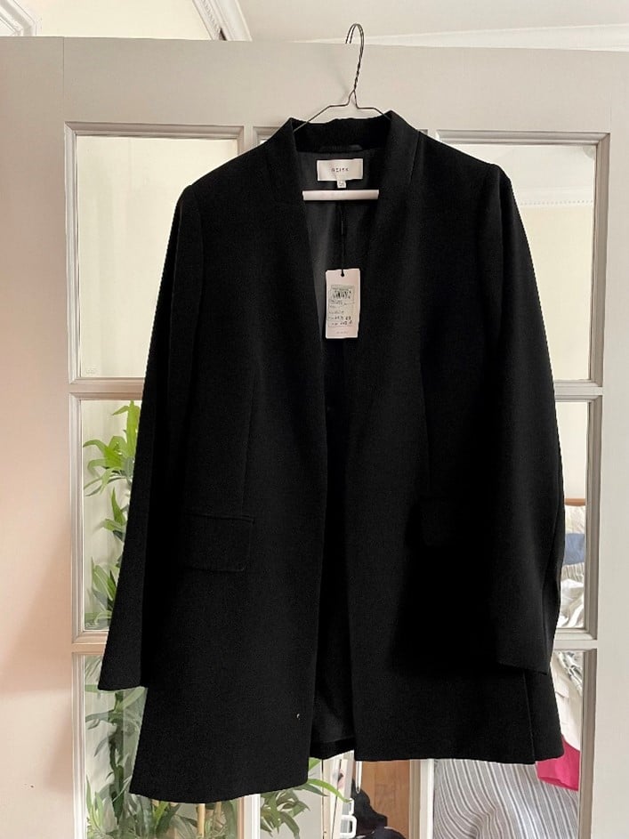 Black open-front blazer coat hanging on a hanger in front of a glass-panel door.