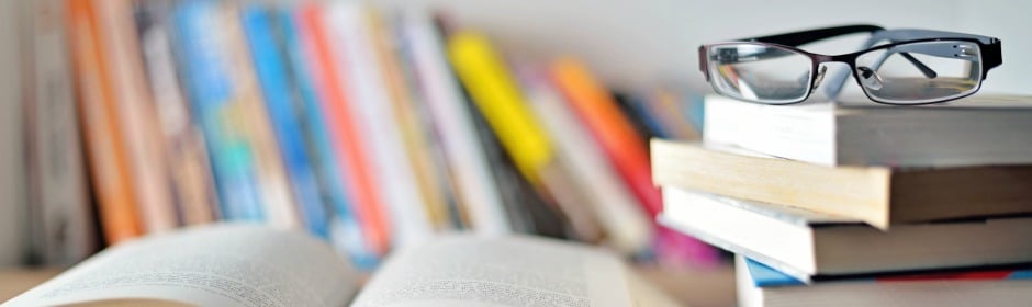 Open book in foreground with a stack of books and reading glasses resting on top.