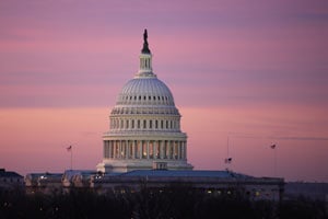 The U.S. Capitol building under a pink-orange sunset sky.