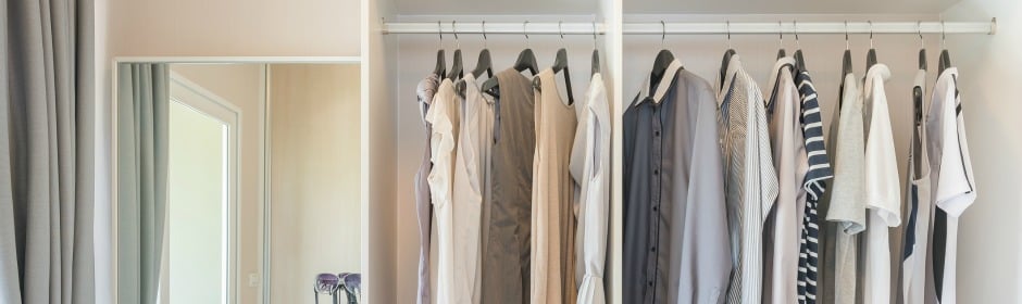 Closet with a row of hanging shirts and jackets in neutral tones, with a mirror on the left.