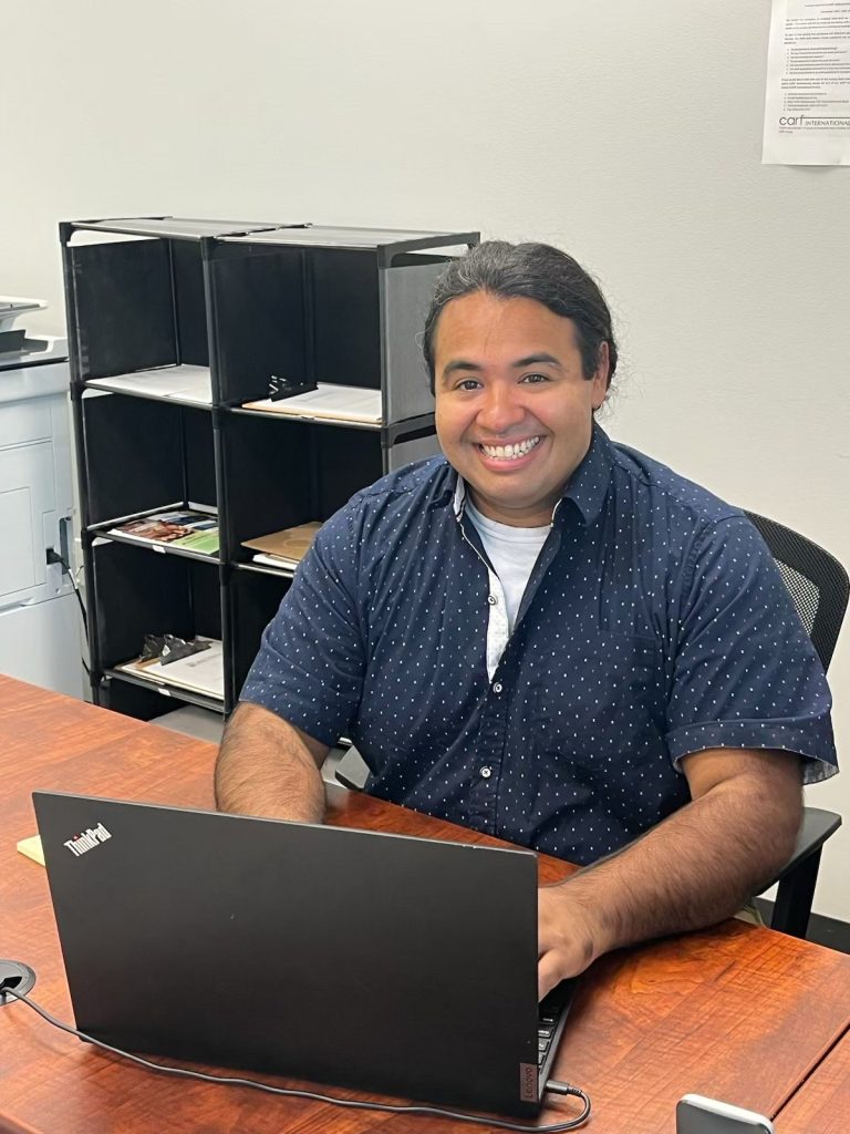 Smiling man seated at a desk with a ThinkPad laptop in a tidy office.