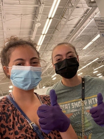 Two shoppers wearing masks and purple gloves giving thumbs up in a store.