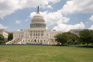Front view of the United States Capitol with steps, dome, and surrounding green lawn under a partly cloudy sky.