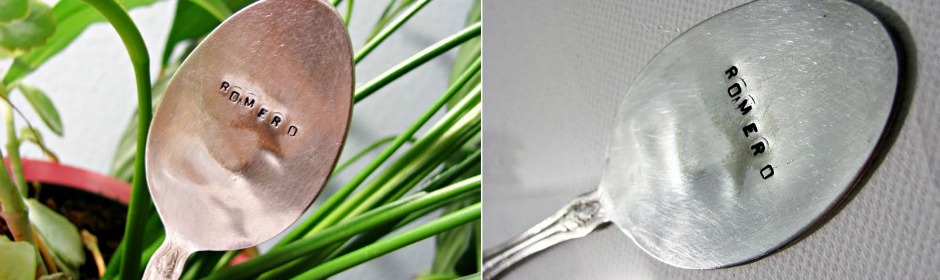 Tarnished silver spoon engraved with 'ROMERD' resting among green plant stems.