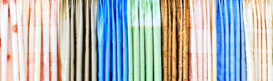 Rows of vibrant fabric rolls hanging side by side in a shop, showcasing a wide color range.