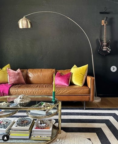 Leather sofa with bright cushions, arc floor lamp, and a wall-mounted guitar in a stylish living room.