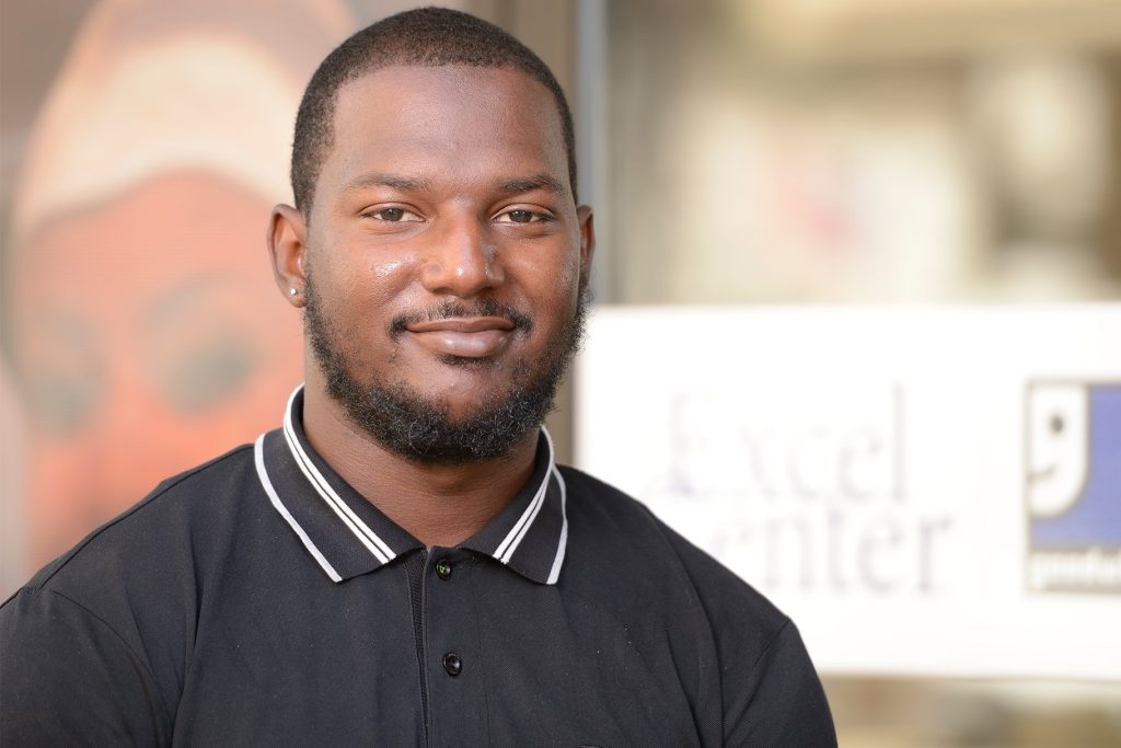Portrait of a smiling Black man with a neatly trimmed beard wearing a black polo shirt.