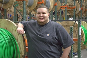 Smiling man in a warehouse standing beside large green cable spools.