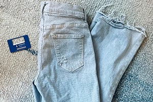Light-wash denim jeans folded on a beige carpet with a blue brand tag attached.