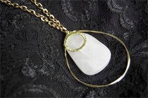 Gold chain necklace with a white teardrop pendant circled by a thin gold ring, displayed on black lace fabric.