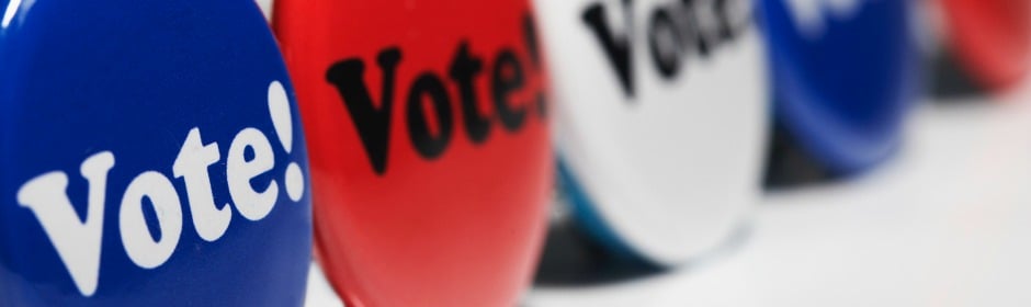 Colorful 'Vote!' buttons arranged in a row, blue, red and white, promoting voting.