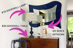 Dresser with a lamp and mirror, wall labels point to a goodwill lamp, goodwill table, and my son's artwork.