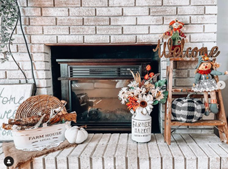 Cozy farmhouse fireplace mantel decorated with pumpkins, floral arrangements, a basket, and a welcome ladder in autumn decor