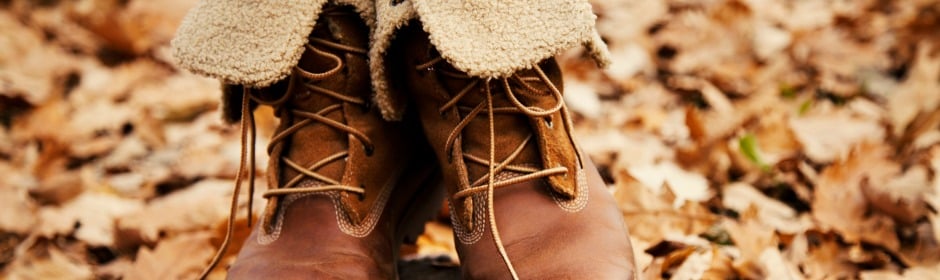 Brown leather hiking boots with tan laces resting on a bed of dried autumn leaves.
