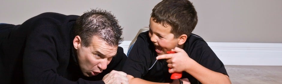 Man and boy lying on the floor laughing; the boy holds a red toy phone to his ear.
