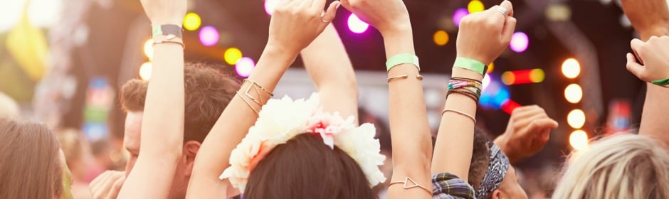 Crowd at a concert with raised hands and colorful stage lights.